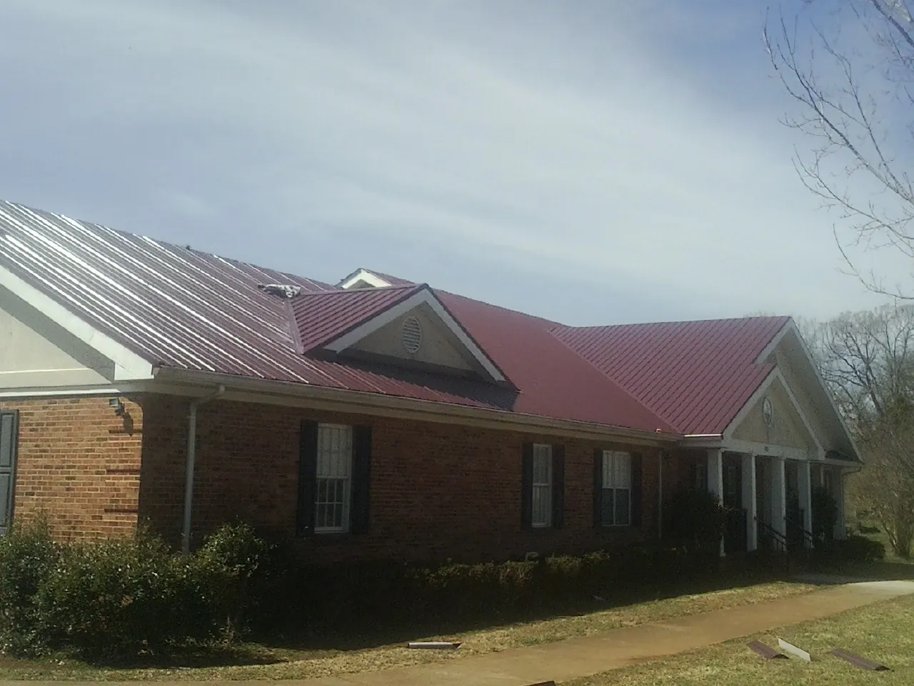 Red metal roof with gabled entries on a long brick building, from a Hail Damage Roof Repair job in East Andover
