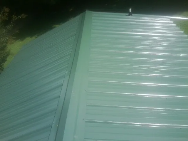 New green metal panels meeting at the ridge of a roof — Flat Roof Repair work by our crew in East Andover