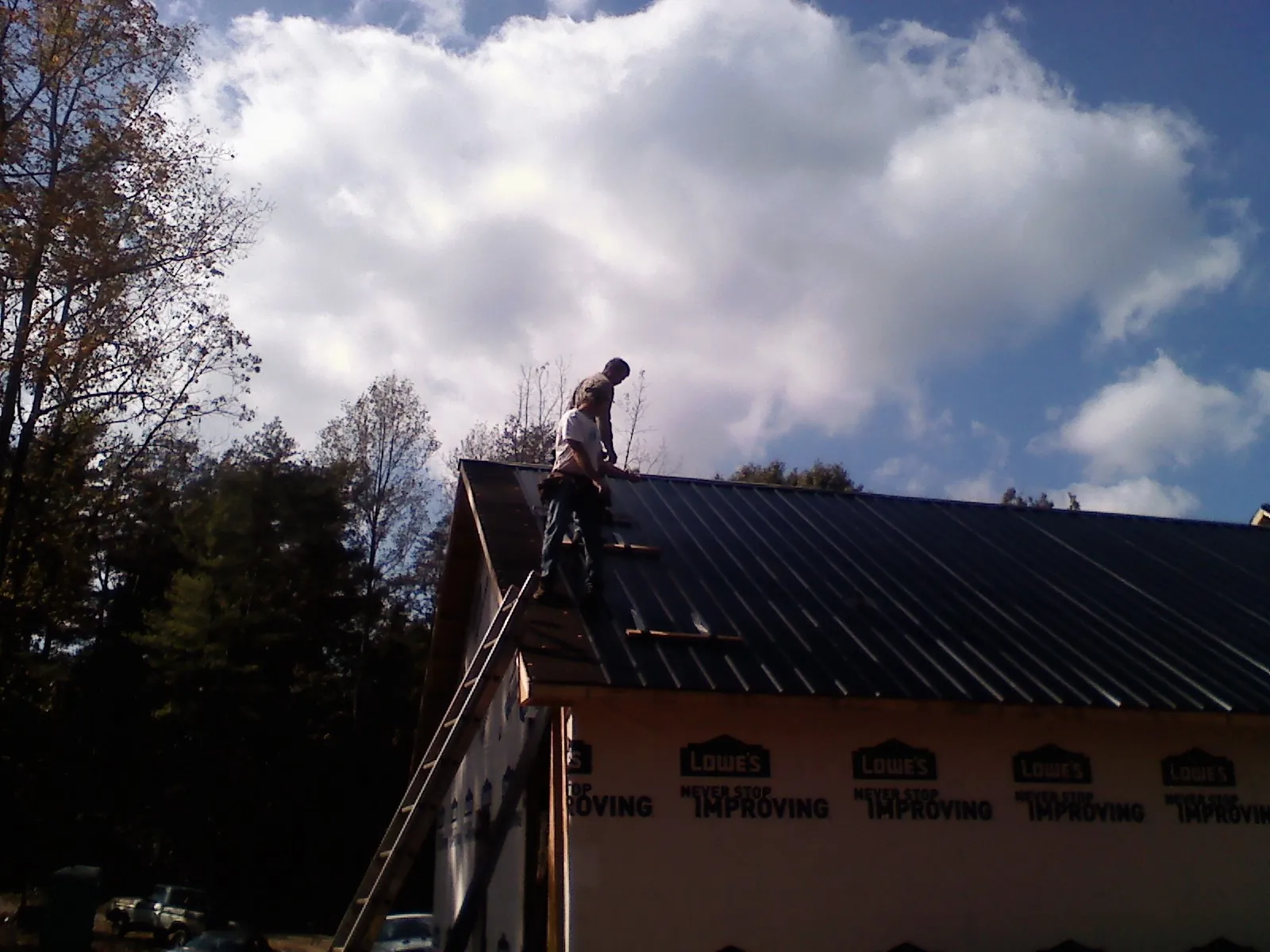 Roofer fastening dark metal panels high against a cloudy sky, from a Roof Inspection job in East Andover