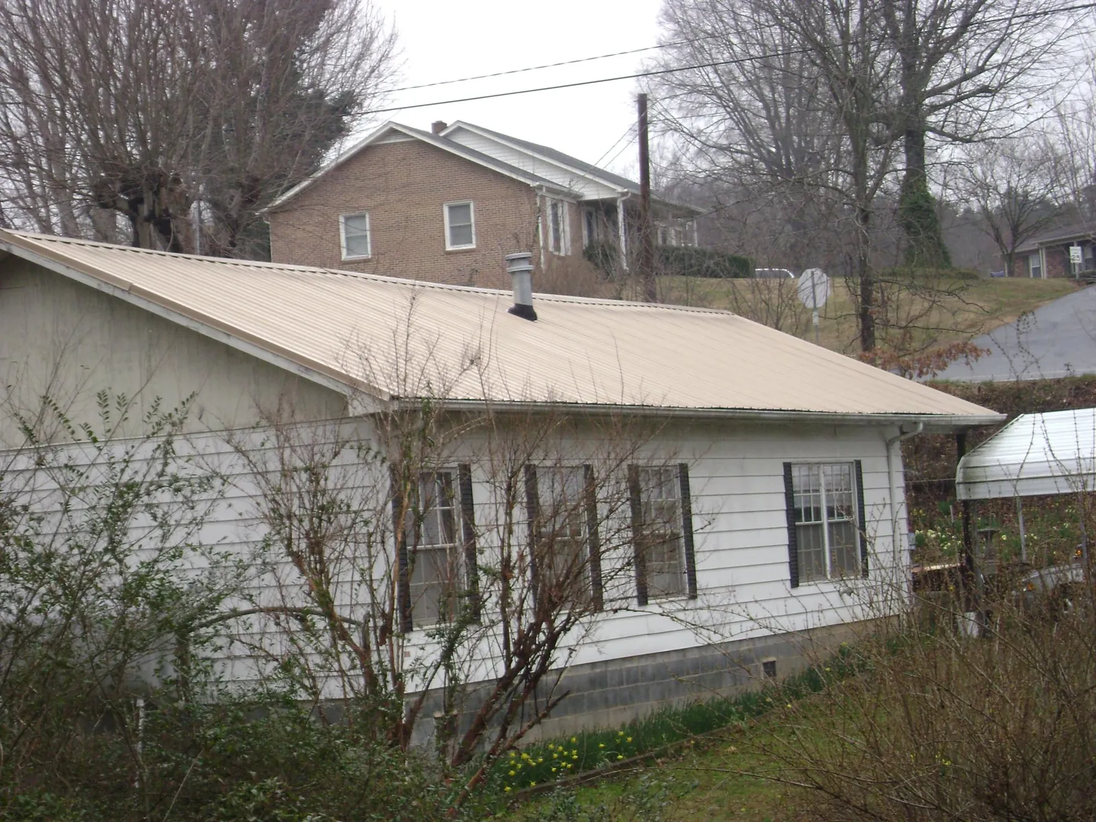 Tan metal roof on a white sided house set into a hillside — Commercial Roofing by Roofing Brothers in East Andover